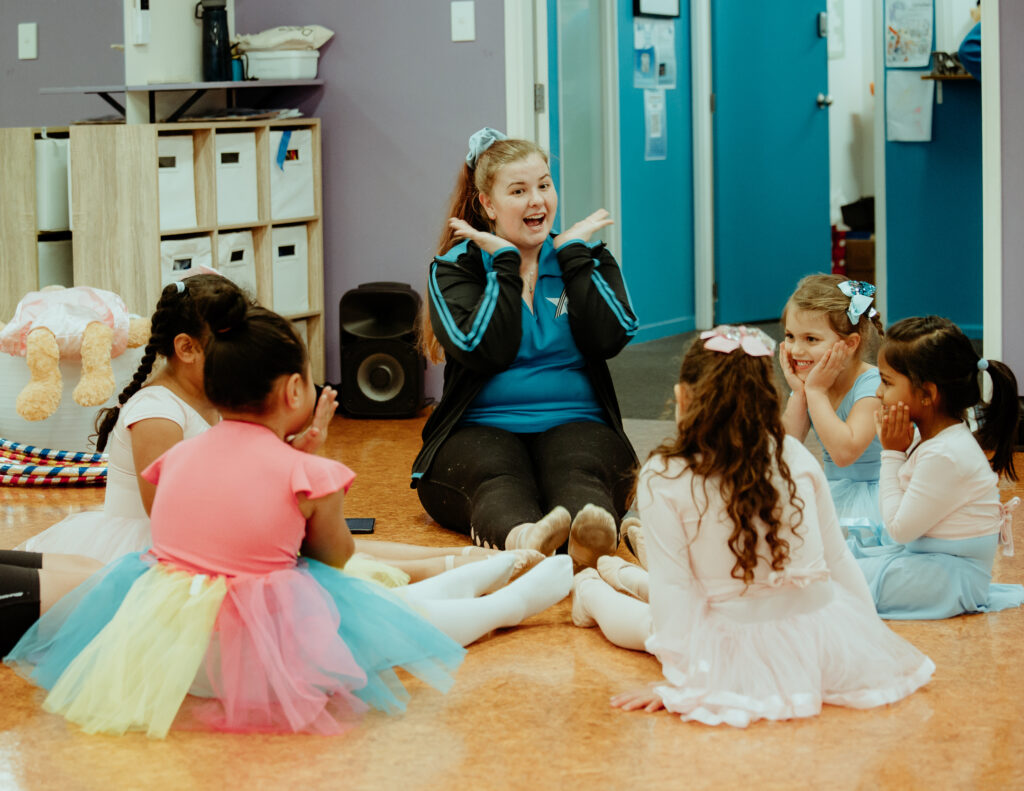 engaging dance teacher with her preschool dance class sitting around her