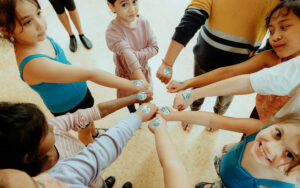 children with their hands together of their circle, showing off their stickers earned from dance class